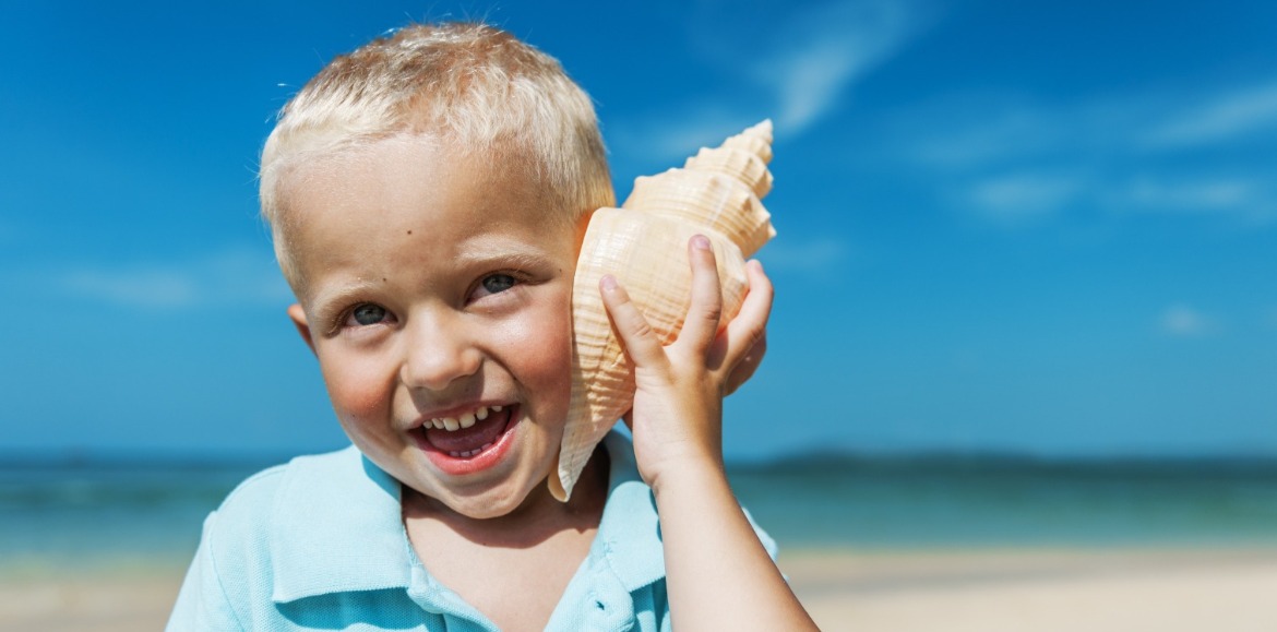 little boy listening to conch shell on the beach | Williamson Realty