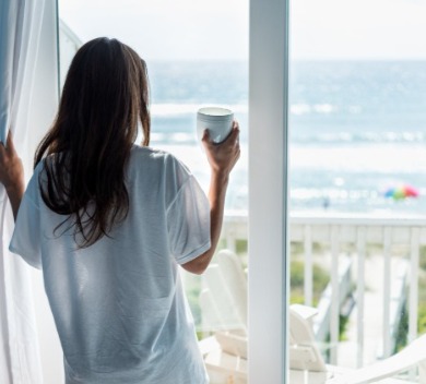 Woman looking out window at the beach with coffee in hand | Williamson Realty Vacations Ocean Isle Beach Rentals