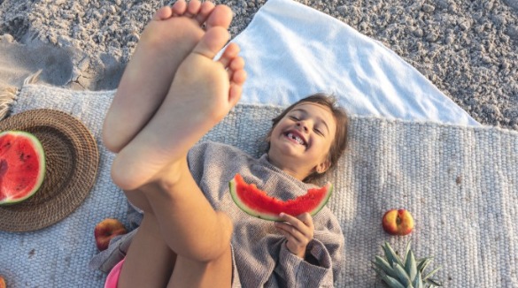 Girl eating watermelon on a beach blanket | Williamson Realty Vacations Ocean Isle Beach Rentals