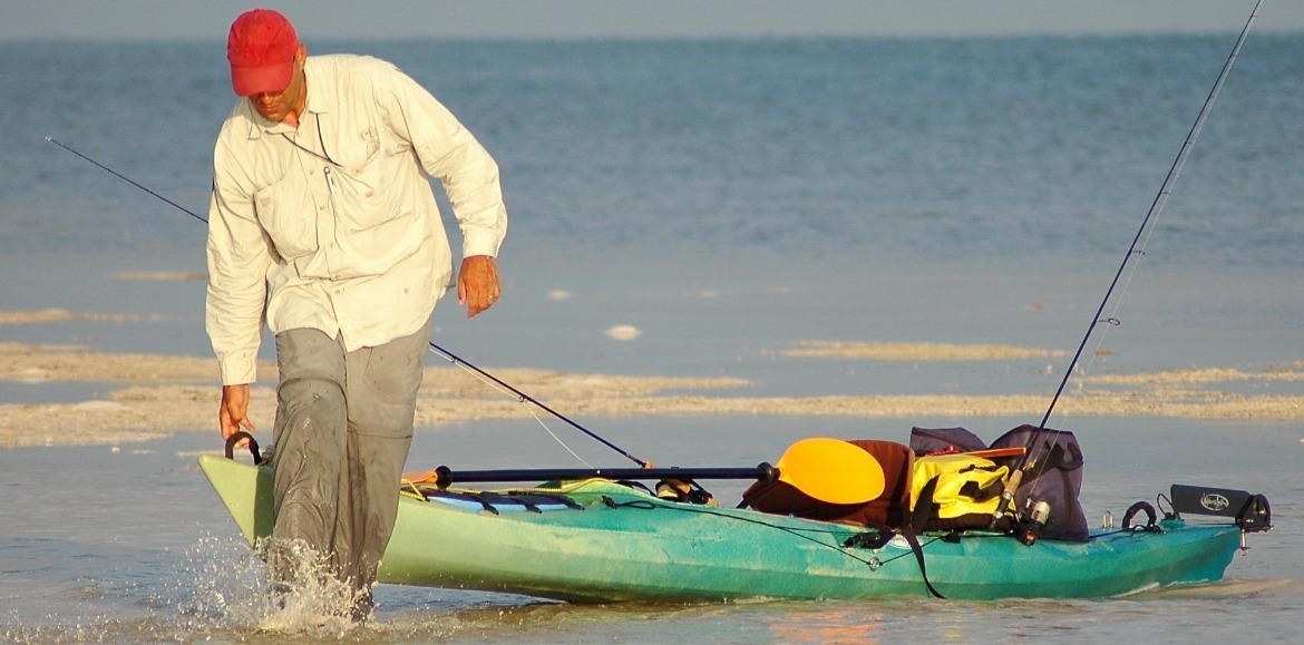 man pulling his fishing kayak out of the water on the beach | Williamson Realty