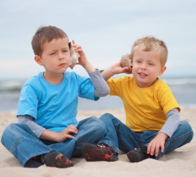 Two young boys on the beach holding seashells to their ears  | Williamson Realty Ocean Isle Beach NC Rentals